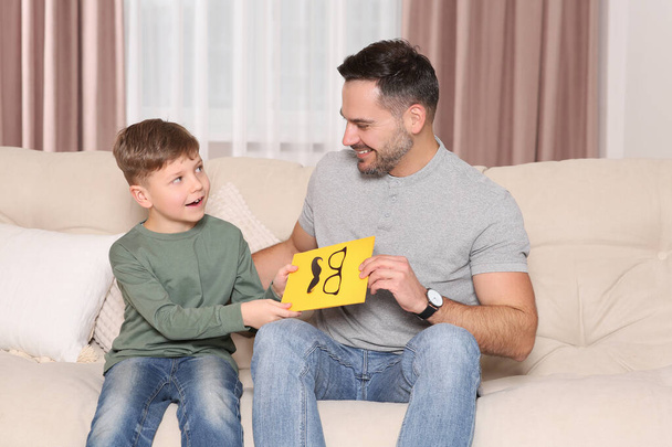 Cute little boy presenting his father with gift on sofa at home - Foto, imagen