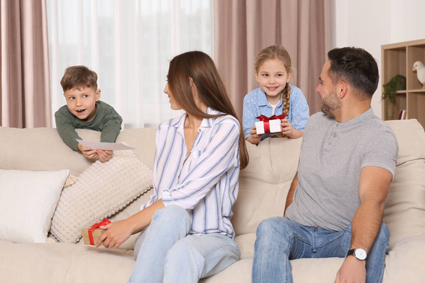 Cute little children presenting their parents with gifts on sofa at home - Фото, зображення