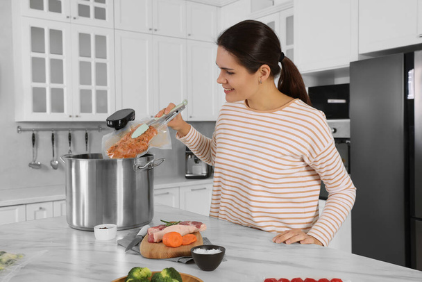 Woman putting vacuum packed meat into pot with sous vide cooker in kitchen. Thermal immersion circulator - Foto, immagini