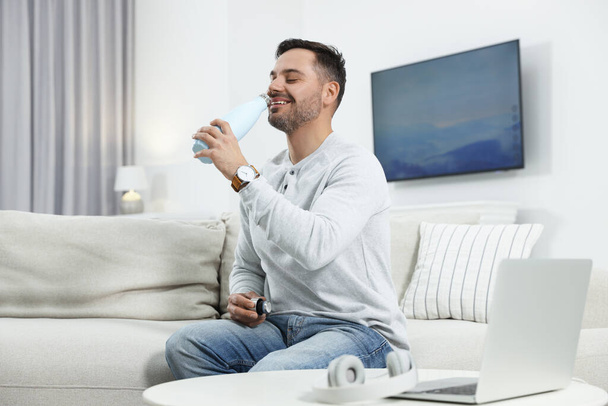 Man drinking from light blue thermo bottle indoors - Foto, Imagen