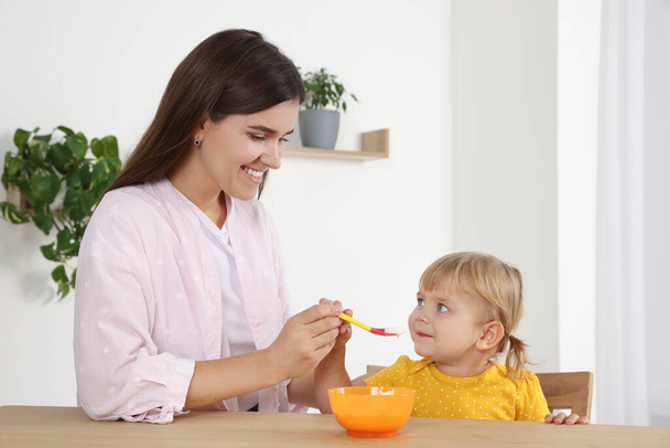 Mother feeding her cute little child with yogurt at wooden table indoors - Foto, immagini