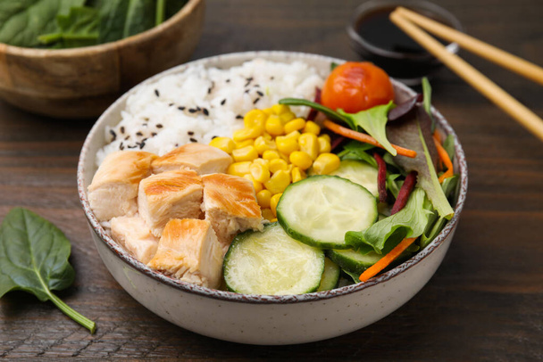 Delicious poke bowl with meat, rice, vegetables and greens on wooden table, closeup - Photo, image