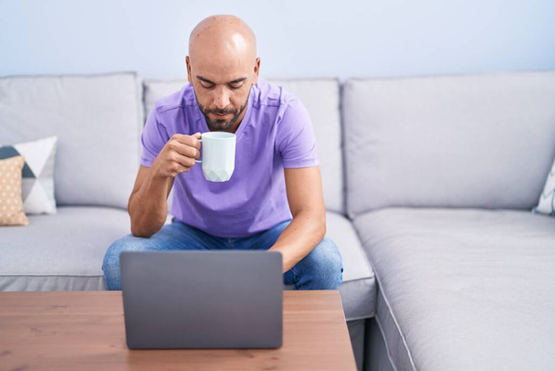 Young bald man using laptop drinking coffee at home - Foto, Bild