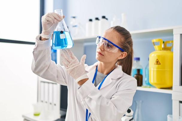 Νεαρή ξανθιά γυναίκα με στολή επιστήμονα που κρατά δοκιμαστικό σωλήνα στο εργαστήριο - Φωτογραφία, εικόνα