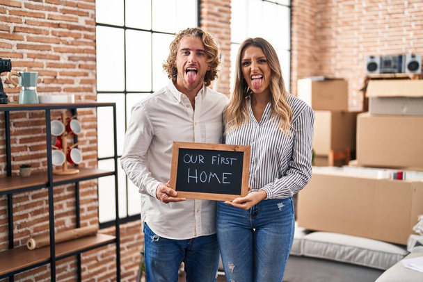 Young couple moving to a new home sticking tongue out happy with funny expression.  - Foto, imagen