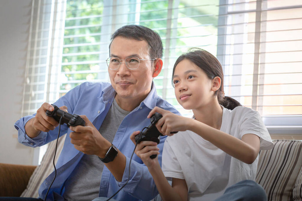 Азіатський батько і дочка грають у відеоігри вдома, люди займаються справами та займаються сімейними ідеями. - Фото, зображення