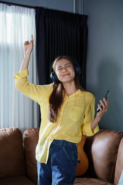 Portrait of asian woman using smart phone mobile and headphones relaxing on sofa at home. - Foto, imagen