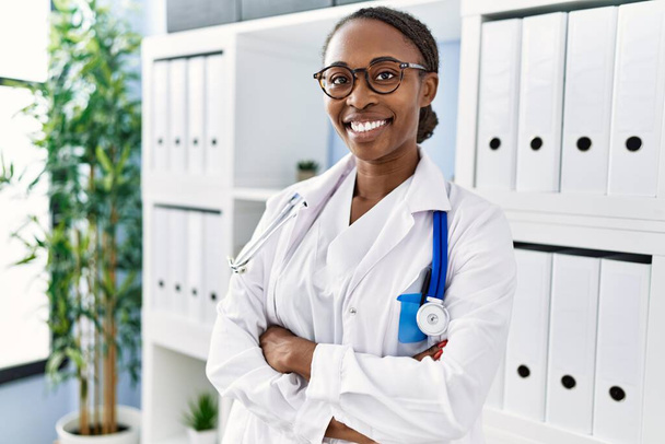 Mujer afroamericana doctora sonriendo confiada de pie con los brazos cruzados gesto en la clínica - Foto, imagen