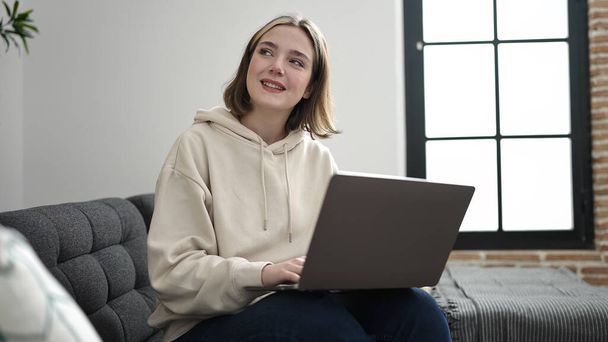 Jovem loira usando laptop sentado no sofá em casa - Foto, Imagem