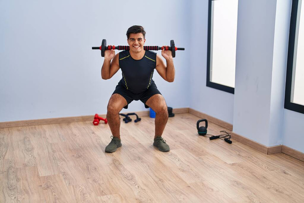 Young hispanic man smiling confident using bar with disc training at sport center - Photo, Image