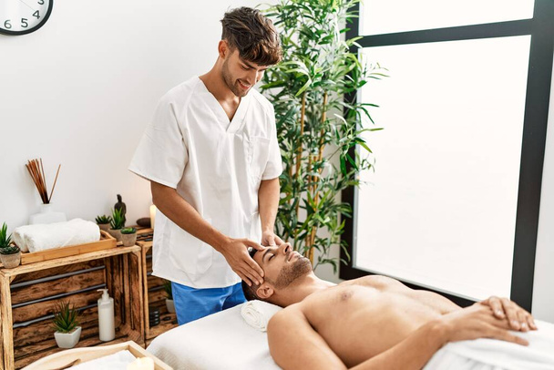 Dois homens hispânicos terapeuta e paciente tendo massagem facial no centro de beleza - Foto, Imagem
