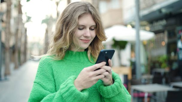 Young blonde woman smiling confident using smartphone at coffee shop terrace - Fotó, kép
