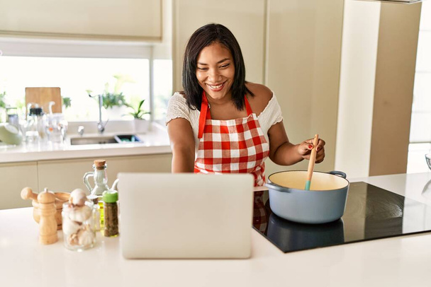 latino brunette vrouw koken op zoek recept op laptop in de keuken - Foto, afbeelding