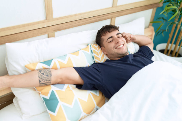 Young hispanic man waking up stretching arms at bedroom - Photo, Image