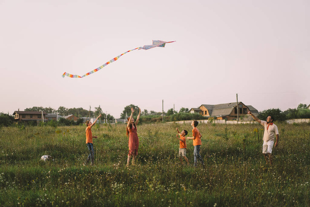 Happy family and children run on meadow with a kite in the summer on the nature. Family playing with kite while running along rural summer field. Family day - Photo, Image