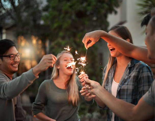 Dont get burned guys. a group of cheerful young friends having fun with sparklers together outside at night - 写真・画像