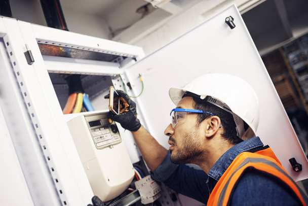 Man, phone and technician in electric inspection for power or sustainable energy at work site. Male electrician, contractor or engineer with smartphone looking to inspect electricity on circuit board. - Photo, Image