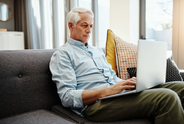 З'єднайтеся з мережею і залишайтеся в курсі. старший чоловік розслабляється і використовує ноутбук на дивані вдома
 - Фото, зображення