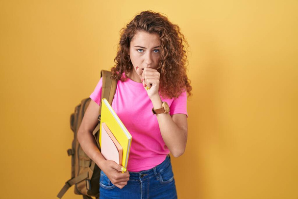 Young caucasian woman wearing student backpack and holding books feeling unwell and coughing as symptom for cold or bronchitis. health care concept.  - Photo, Image