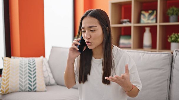 Mladá krásná hispánská žena mluví na smartphonu s nešťastným výrazem doma - Fotografie, Obrázek