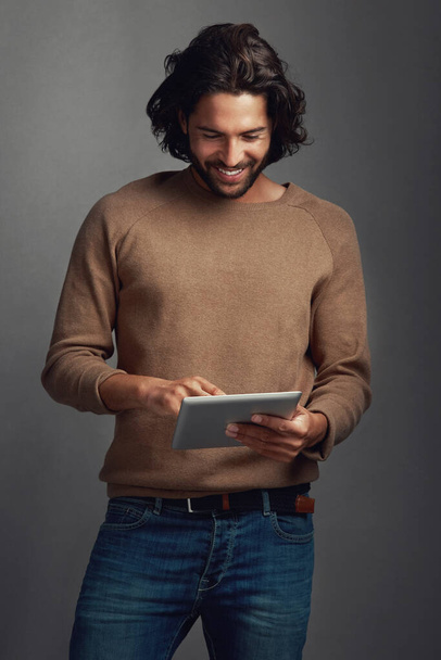 Felicidad inspirada en internet. Captura de estudio de un joven guapo usando una tableta digital sobre un fondo gris - Foto, imagen