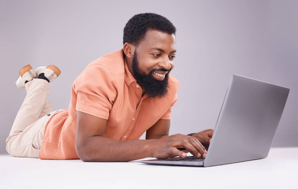 Happy black man, laptop and studio floor to search social media, online shopping or subscription download. Smile, male model and computer technology for internet, typing email or elearning on website. - Фото, изображение