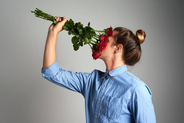 Зупиніться і відчуйте запах троянд. Студійний знімок невпізнаваного чоловіка, що тримає квіти на сірому фоні
 - Фото, зображення