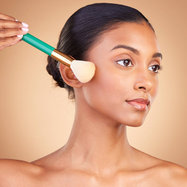 Makeup, cheek and brush with indian woman in studio for foundation, blush and self care. Glow, cosmetics and facial with female model isolated on brown background for shine, clean and confidence. - Zdjęcie, obraz