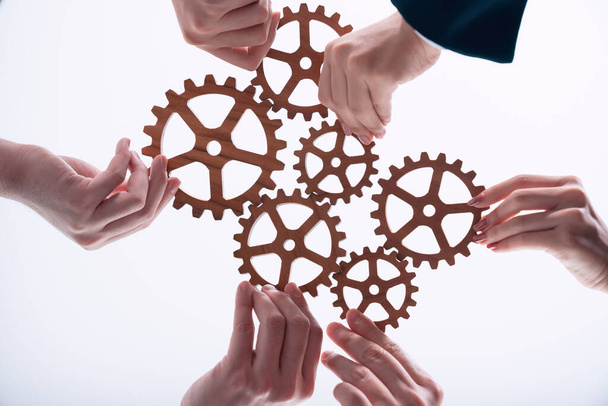 Hand holding wooden gear by businesspeople wearing suit for harmony synergy in office workplace concept. Isolated background. Bottom view of people hand make chain of gear into collective unity symbol - Foto, immagini