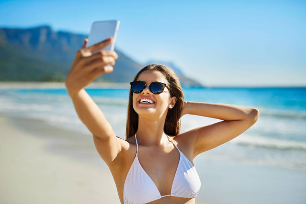Beter dan een selfie met uitzicht. een mooie jonge vrouw neemt een selfie op het strand - Foto, afbeelding