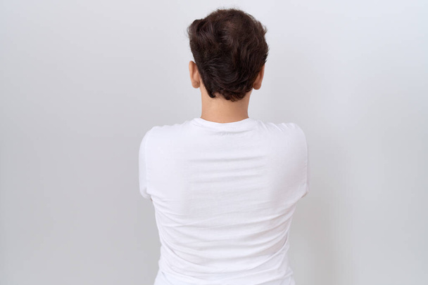 Νέοι μη δυαδικό άνθρωπος φορώντας casual λευκό t πουκάμισο στέκεται πίσω κοιτάζοντας μακριά με σταυρωμένα χέρια  - Φωτογραφία, εικόνα