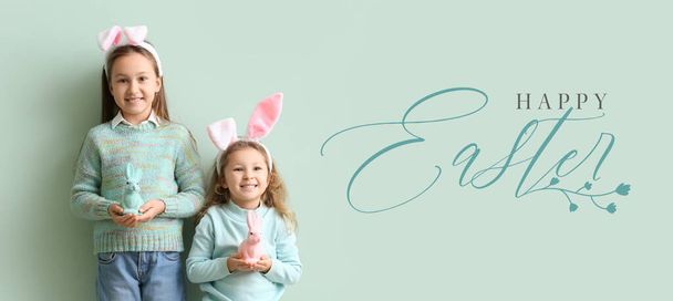 Greeting card with little girls holding figures of Easter bunnies on mint background - Fotoğraf, Görsel