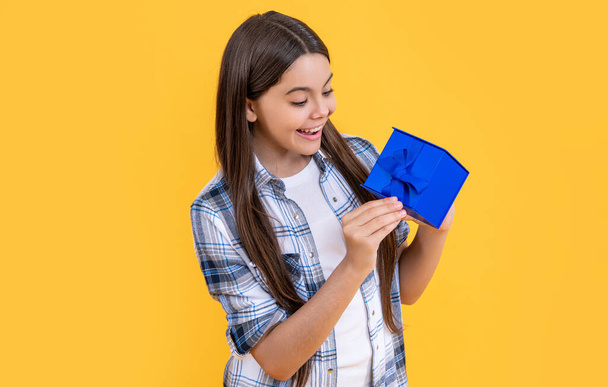 curious teen girl with birthday gift on background. photo of teen girl with birthday gift box. teen girl with birthday gift isolated on yellow. teen girl with birthday gift in studio. - Foto, imagen