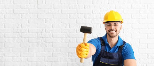 Trabalhador masculino com martelo de borracha no fundo de tijolo branco com espaço para texto - Foto, Imagem
