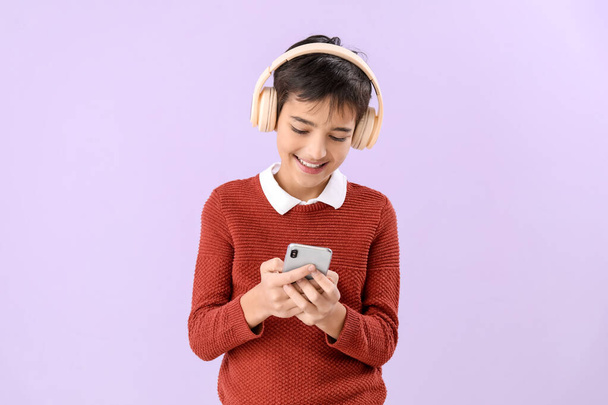 Niño en auriculares con teléfono móvil sobre fondo lila - Foto, Imagen