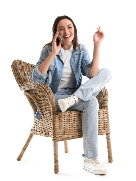 Молода жінка розмовляє мобільним телефоном у плетеному кріслі на білому тлі
 - Фото, зображення
