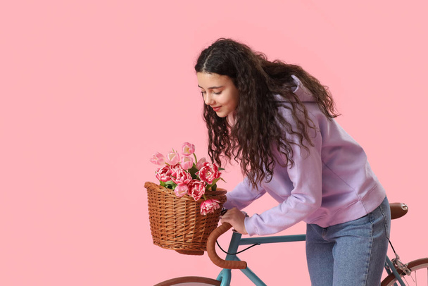 Teenage girl with bicycle and flowers on pink background - Photo, Image