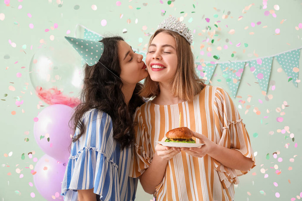 Ευτυχισμένες νεαρές γυναίκες με burger γιορτάζει γενέθλια σε πράσινο φόντο - Φωτογραφία, εικόνα