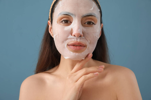 Young woman with sheet mask on blue background, closeup - Photo, Image