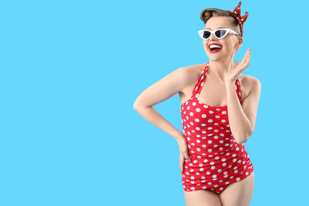 Young pin-up woman in polka dot swimsuit on blue background - Photo, image
