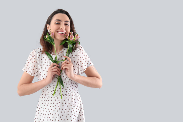 Young woman in dress with alstroemeria flowers on grey background - Foto, Imagem