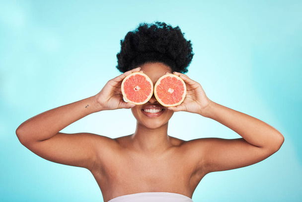 Black woman, face and smile with grapefruit for skincare nutrition, beauty or vitamin C against a blue studio background. Portrait of African female smiling with fruit for natural health and wellness. - Valokuva, kuva