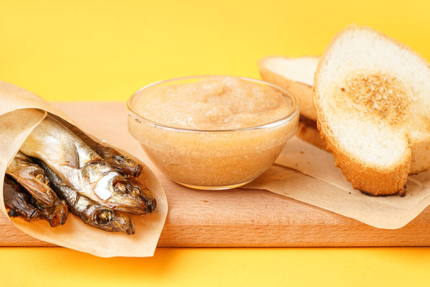Bowl with caviar, smoked capelin wrapped in parchment and fried baguette on yellow background - Photo, Image