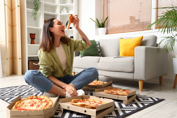 Beautiful woman with boxes of tasty pizza sitting on floor at home - Fotó, kép