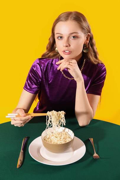 Молодая женщина с миской китайской лапши за столом на желтом фоне - Фото, изображение