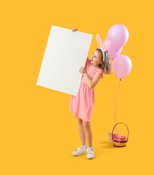 Little girl in bunny ears with blank poster and balloons on yellow background - Fotoğraf, Görsel