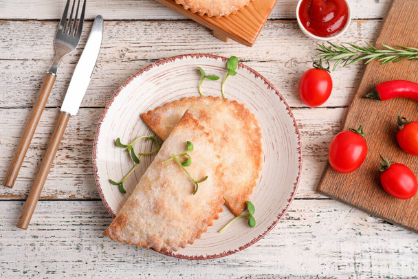 Plate with baked meat empanadas, sauce and vegetables on light wooden background - Photo, Image