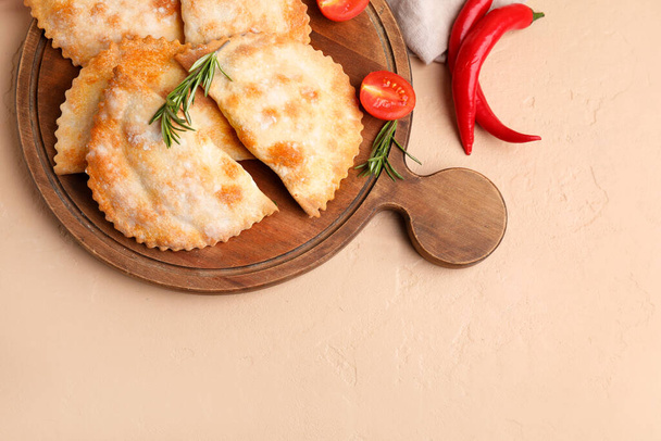 Wooden board with baked meat empanadas and vegetables on color background - Photo, Image