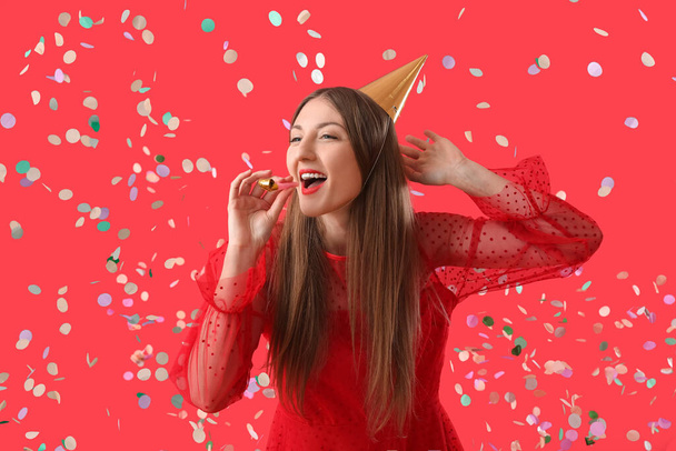 Happy young woman with party blower celebrating Birthday on red background - Fotoğraf, Görsel