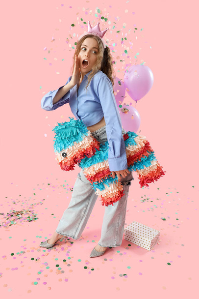 Mujer joven sorprendida con piñata celebrando cumpleaños sobre fondo rosa - Foto, Imagen